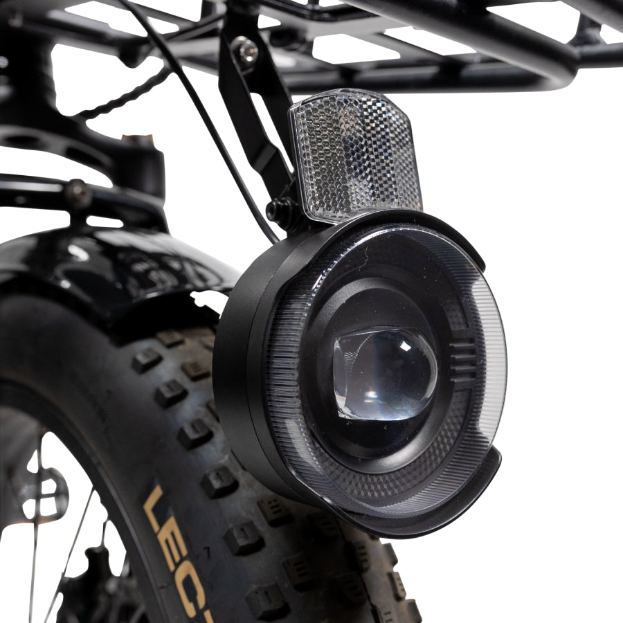 close-up of an Elite headlight accessory installed a front rack turned off with a Lectric tire behind it against a white background