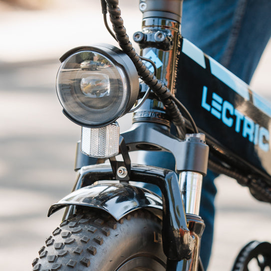 close-up of the elite headlight accessory installed on a Lectric eBike turned off outside during the day with a rider appearing in the background