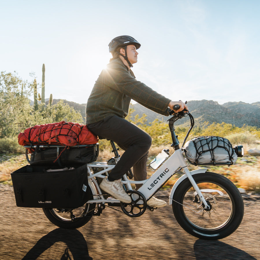 Man with bike helmet riding Lectric XPedition cargo eBike carrying camping supplies in desert