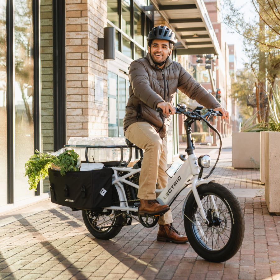 Man in a bike helmet riding Lectric XPedition cargo ebike carrying a case of water and groceries