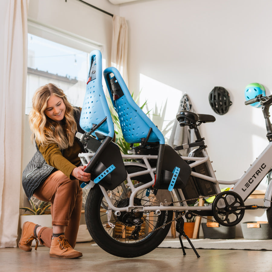 Woman attaching two Yepp seats to the back of her Lectric XPedition cargo ebike in a room