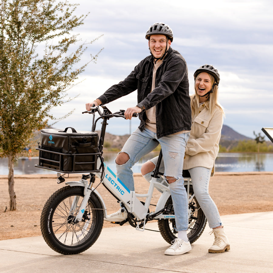 Man riding an ebike in the park with a woman as a passenger and a soft cooler in the front basket