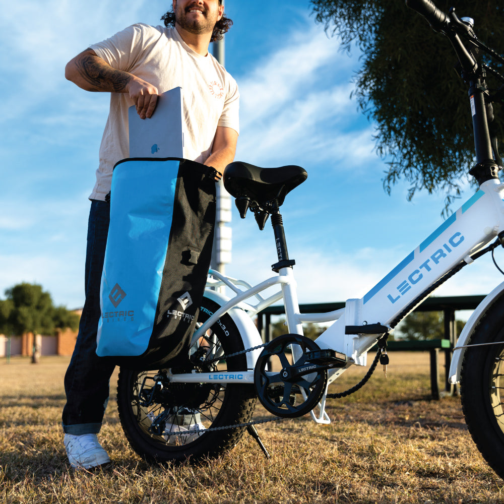 Man in the park placing a laptop in a waterproof pannier bag on an electric bike